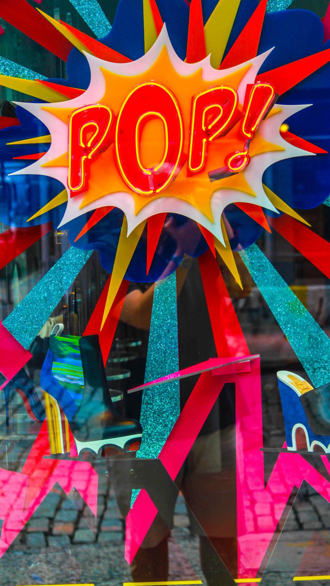Neonlicht mit dem Schriftzug 'Pop' in Rot-Gelb auf einer bunten Glasscheibe.