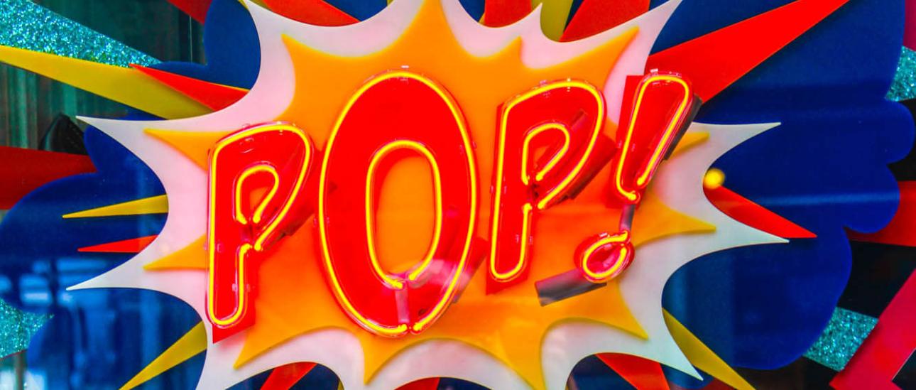 Neonlicht mit dem Schriftzug 'Pop' in Rot-Gelb auf einer bunten Glasscheibe.